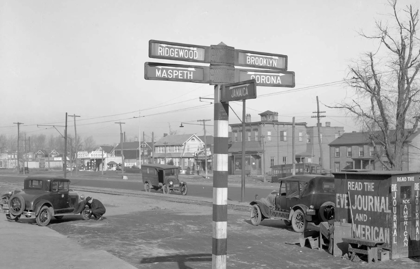 1931 photo of a signpost at the corner of Queens Boulevard and Grand Avenue pointing the way to Ridgewood, Brooklyn, Maspeth, Corona, and Jamaica 