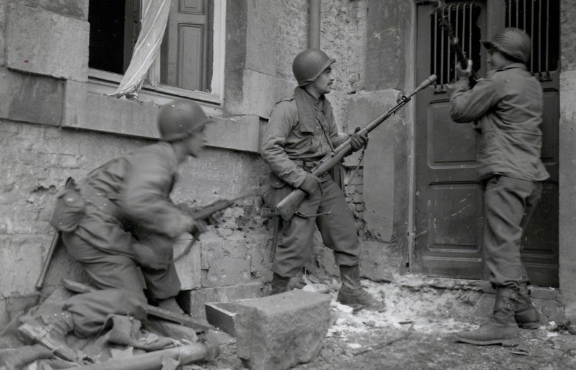 Three Americans of the 117th Infantry Regiment are about to enter a house where several enemy snipers are holding out.